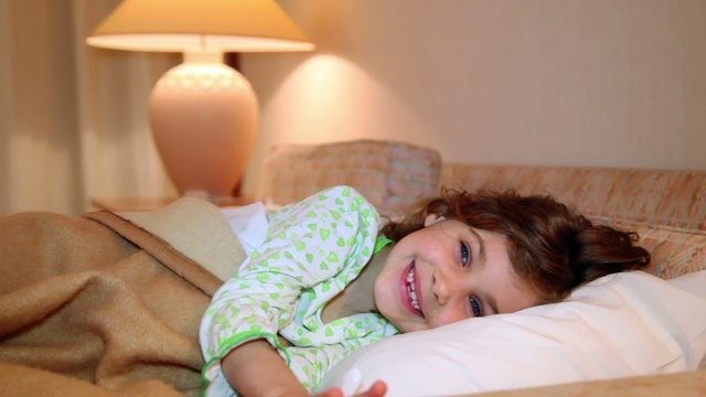 Little girl wakes and smile in bed at background of lamp