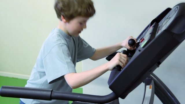 Little boy walks on treadmill and looks to panel with hands on