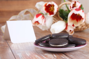 Tulips, chocolate cookies and blank card on a wooden board