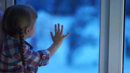 Child looking at playground winter. Snow falls on the street