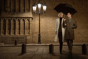 Elegant couple with umbrella outdoors on rainy evening