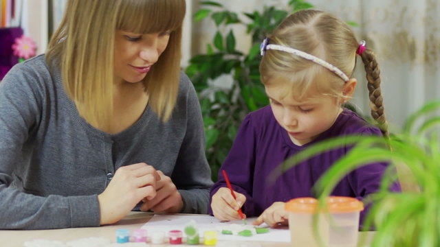 Mother teaches a child to paint. The girl is engaged in drawing