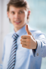 Happy smiling young business man with thumbs up gesture at his o