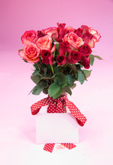 Blank paper on red ribbon with roses in vase