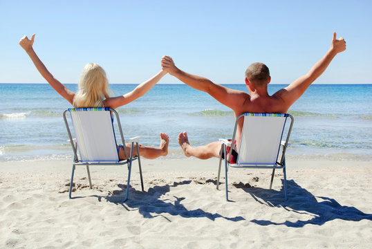 Positive young couple sitting on the beach chair on the sea beac