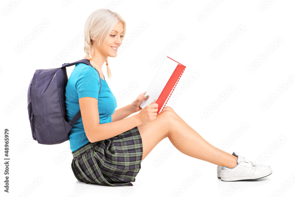 Wall mural A smiling student reading a book and sitting on a floor