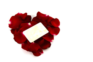 Red rose petals in a heart shape and old card isolated on white
