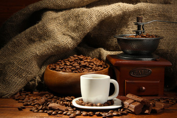Coffee grinder and cup of coffee on burlap background