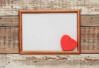 A red heart in an old wooden frame on an old rough wall.
