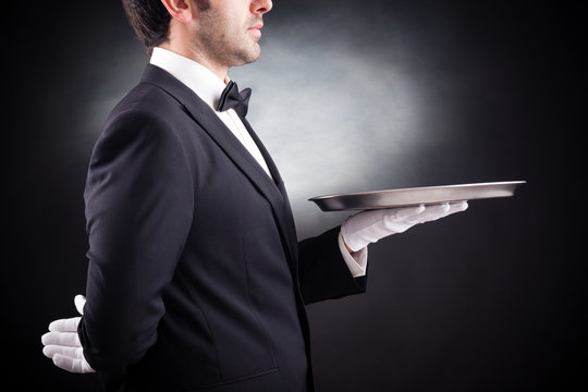Cropped image of a young waiter holding an empty dish on black b