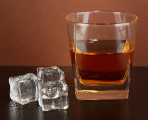 Glass of whiskey and ice on brown background