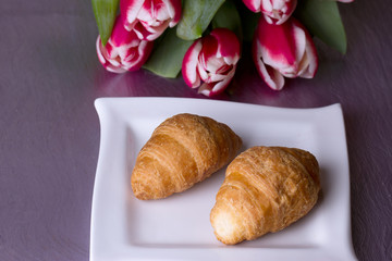 Two croissants  next to a bouquet of tulips