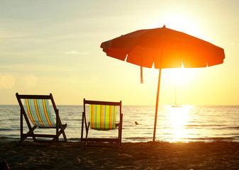 Pair of beach loungers on the deserted coast sea at sunrise.