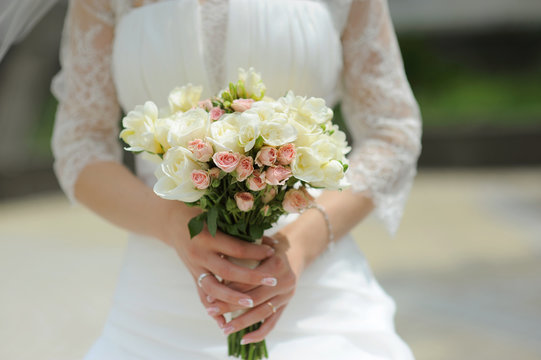 bride holding white roses bouquet in park