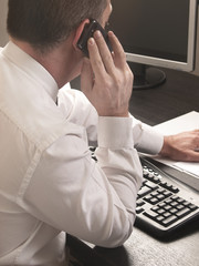 Hombre hablando por teléfono y trabajando junto a un ordenador. Vista de frente y de cerca