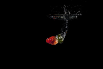 Fresh fruit dropped into water with splash on black background