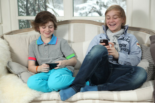 Two boys sitting on the couch and playing with her Handy