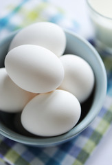 Bowl full of eggs with milk out of focus in background.