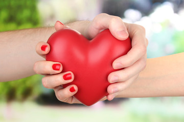 Fototapeta na wymiar Czerwone serce na dłoni kobiety i mężczyzny, na zielonym tle