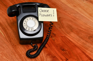 Black retro telephone with reminder note to order flowers