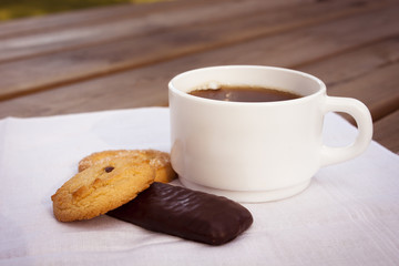 Cup of coffee with cookies and chocolate on wooden table.
