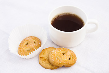 Cup of coffee with cookies on white cloth.