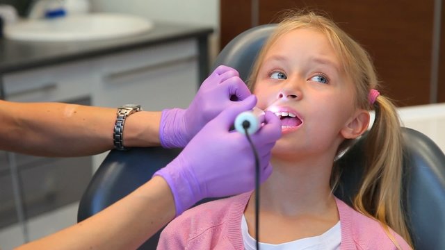 Woman dentist diagnoses teeth of little girl patient