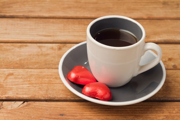 Coffee cup with heart shape chocolate on wooden background