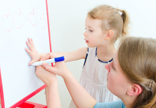 Pretty little girl with teacher near whiteboard