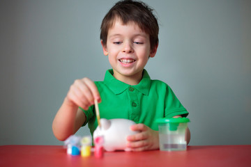 Cute happy little boy painting his piggy toy