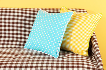 Colorful pillows on couch on yellow background