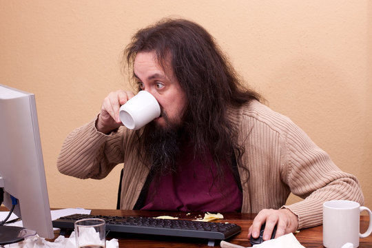 Nerd schaut konzentriert auf Monitor und trinkt aus Tasse