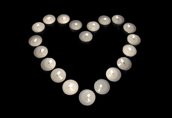 Group of burning candles forming a heart  on black isolated.