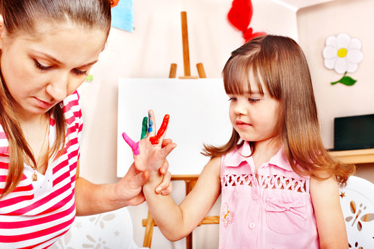 Child painting  with teacher in preschool.