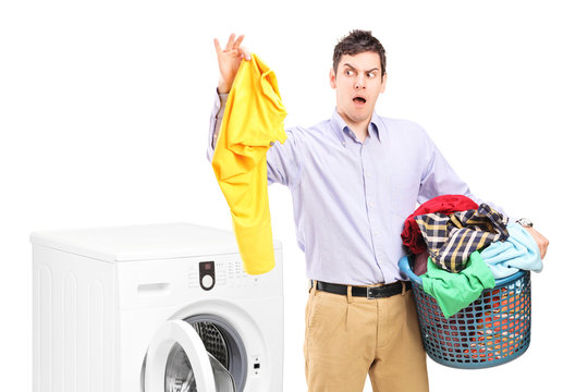 Young man standing next to a washing machine and holding dirty l
