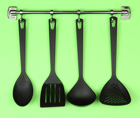 Black kitchen utensils on silver hooks, on green background