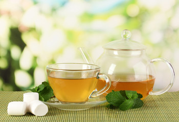 Cup of tea with mint on table on bright bacground