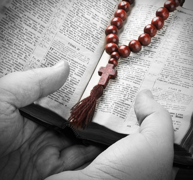 hands holding the Bible and praying with a rosary