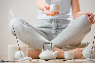 Woman sitting on floor of her home and holding tea cup. Aromathe