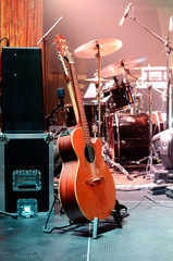 Acoustic guitar, drum kit, loudspeaker and other musical equipment on stage before concert. Red...