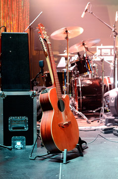 Acoustic guitar, drum kit, loudspeaker and other musical equipment on stage before concert. Red light. Concept image. Night club, performance, music band, singing, profession, art, instrument