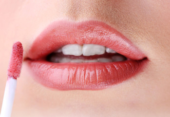 Beautiful young woman applying lip gloss, close up.