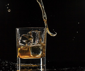 Pouring whiskey into glass, isolated on black background