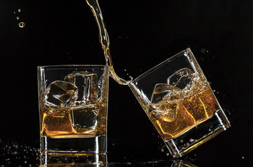 Pouring whiskey into glasses, isolated on black background