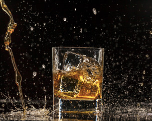 Whiskey splashing around glass, isolated on black background