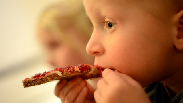Zwei kleine Kinder auf dem Sofa essen ein Brot