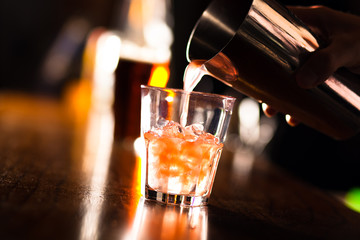 Hands of a bartender pouring a drink into a glass - obrazy, fototapety, plakaty