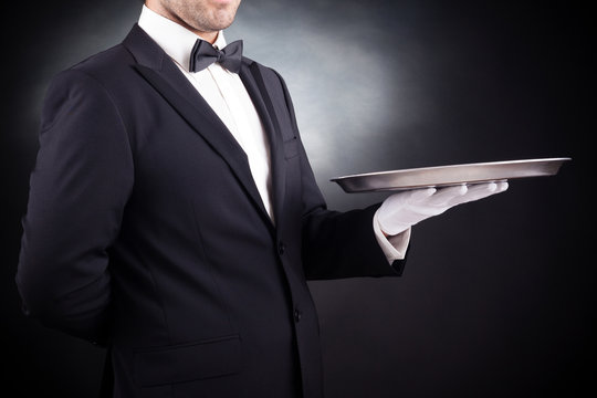 Image of a young waiter holding an empty dish on black backgroun
