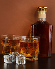Bottle and Glasses of whiskey and ice on brown background