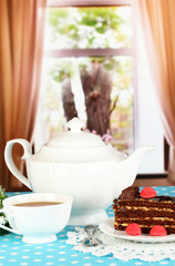 Teapot, cup of tea and delicious cake on window background
